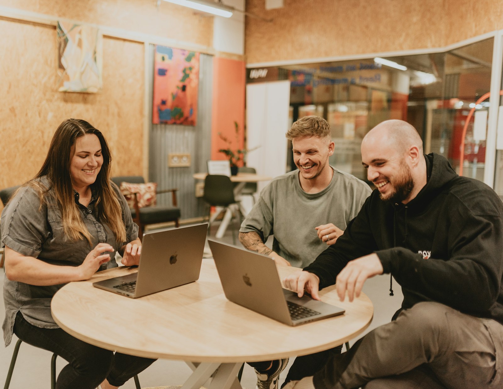 Three people laughing together while they work on laptops at a table
